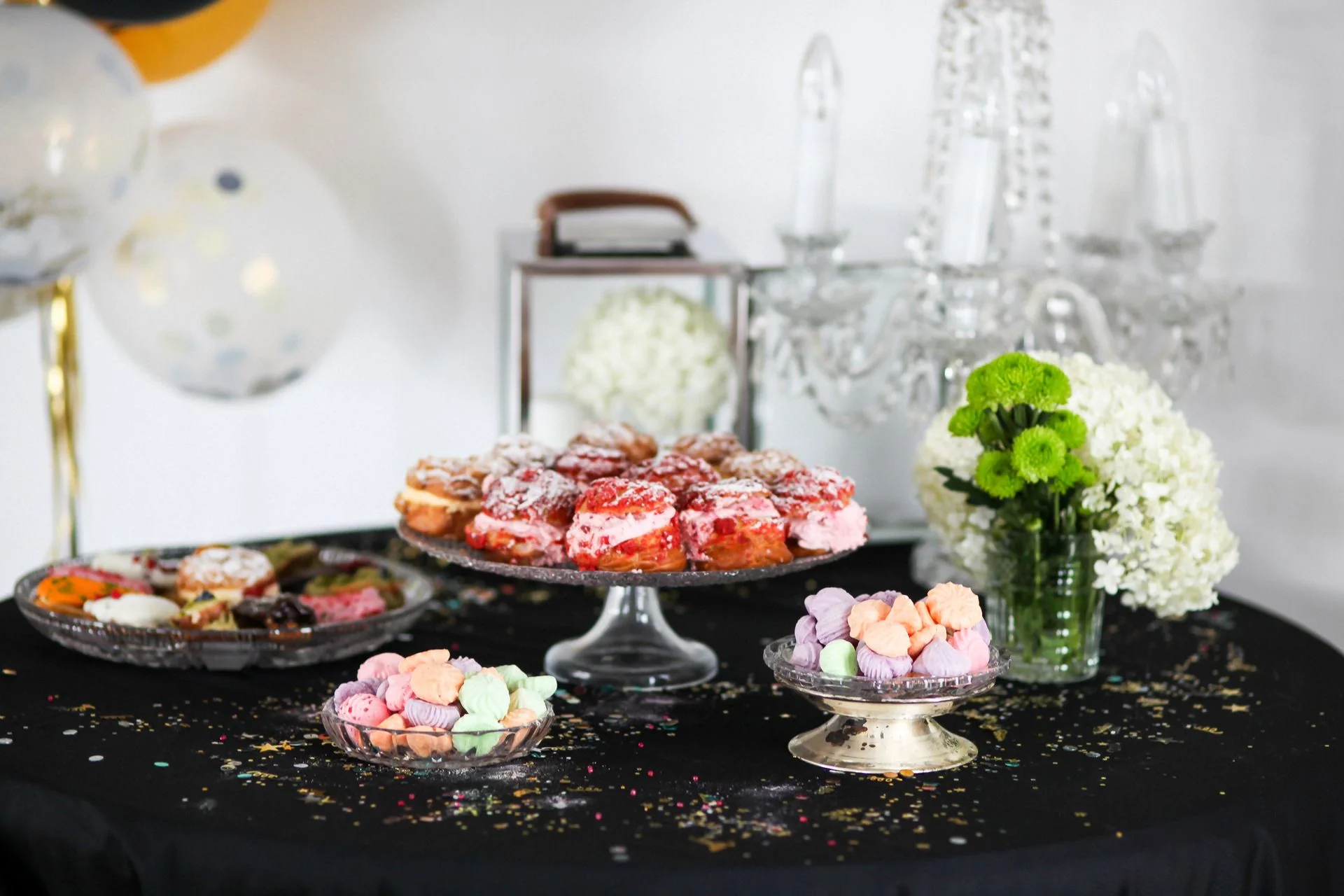 Dessert table with pastries and meringues on glass stands beside white flowers