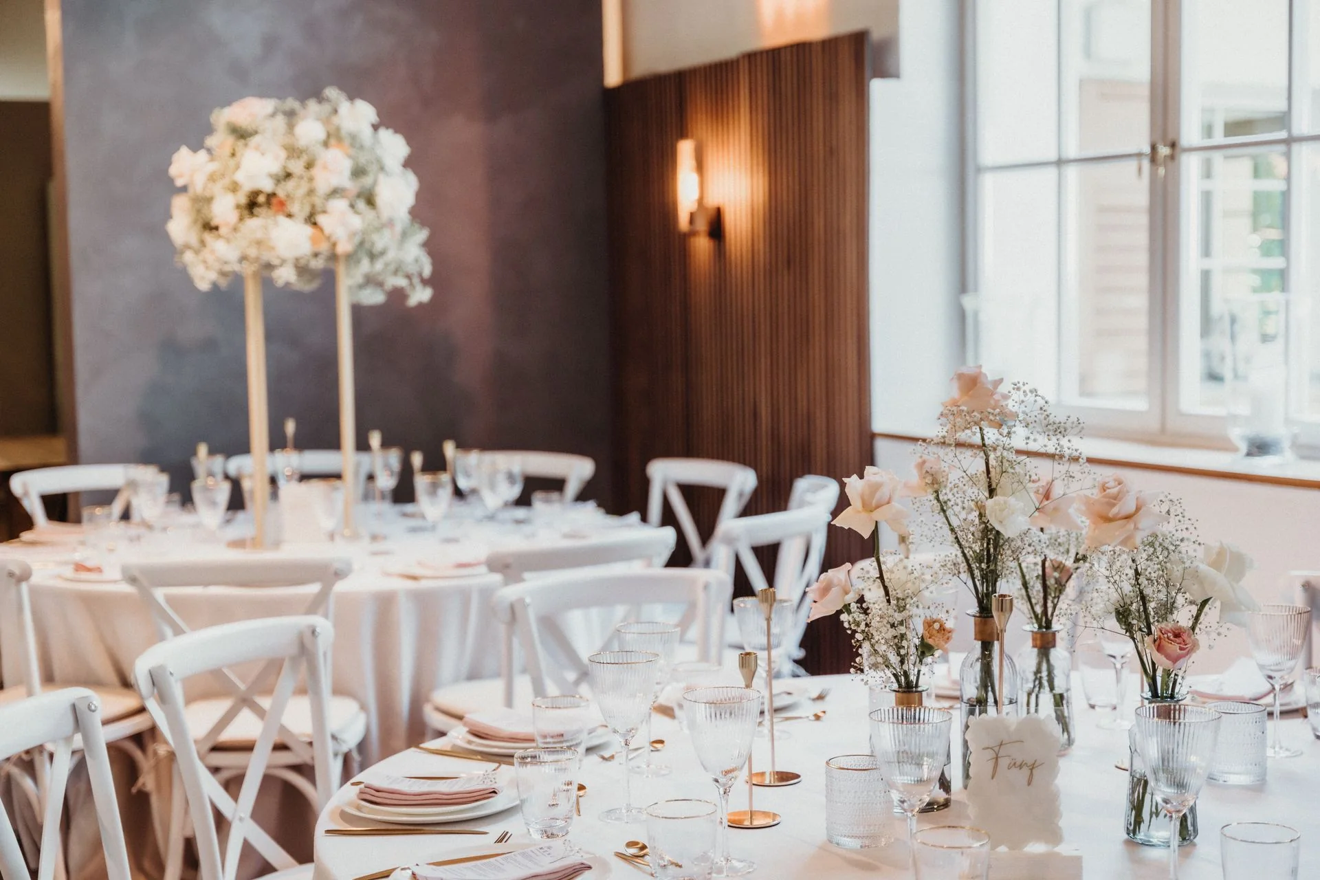 Wedding reception tables with white linens, tall floral centrepieces and candles